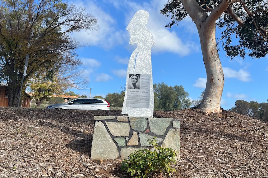 A silver statue in the shape of a nurses silhouette sits on a rock wall.