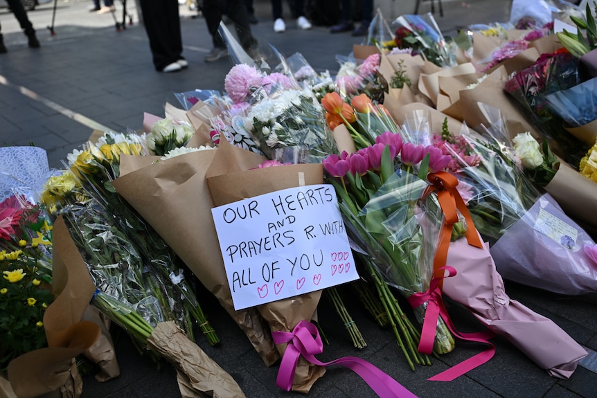 Flower bunches on a street with a sign telling victims they're been thought of