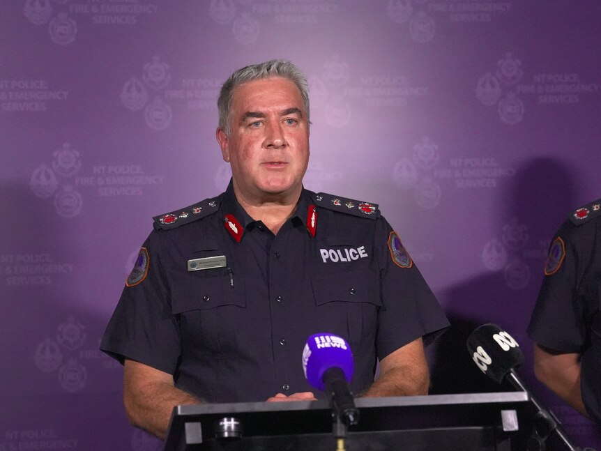 a middle-aged male police officer in uniform speaking at a lectern