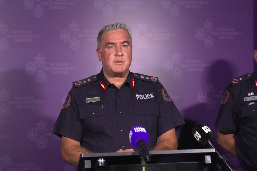 a middle-aged male police officer in uniform speaking at a lectern