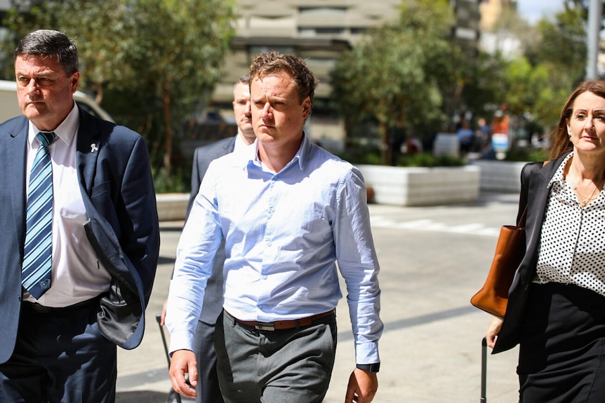 Brent Wyndham in a pale shirt, walking with lawyers.