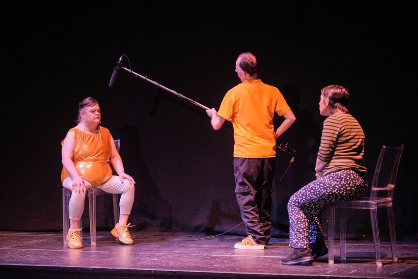 Three people on a stage, one holding a boom mic.
