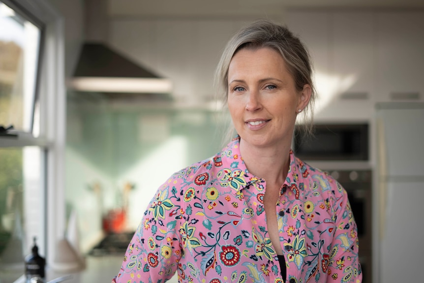 A portrait of a blonde-haired woman wearing a pink button-up shirt.