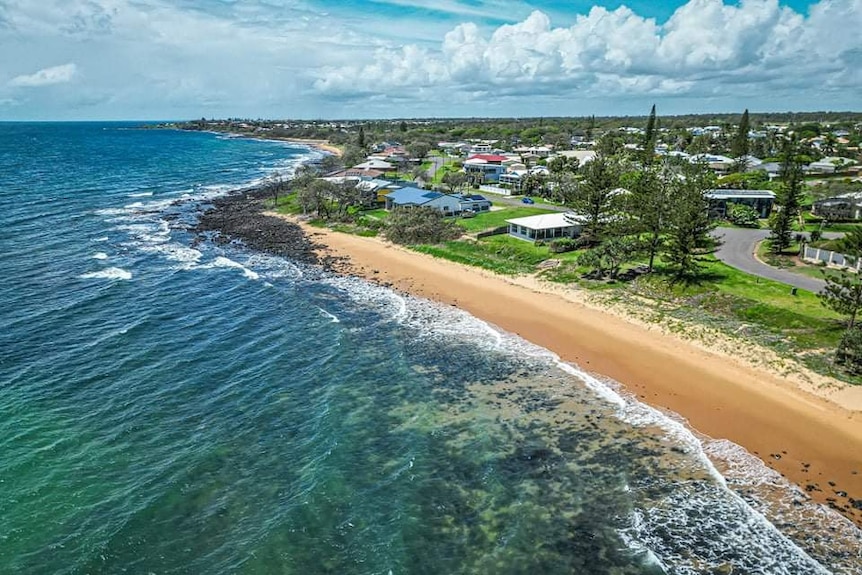 An aerial photo of the ocean and beach in the foreground and houses along the coast