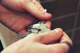 A close-up shot of a person's hands holding a set of silver house keys.