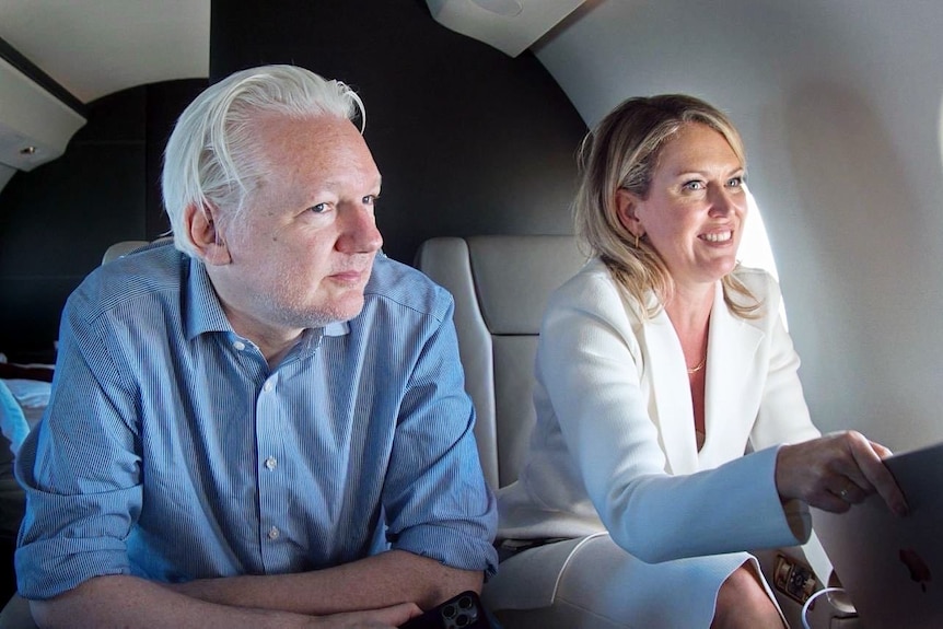 Assange and Robinson sit in plane seats, looking happy.