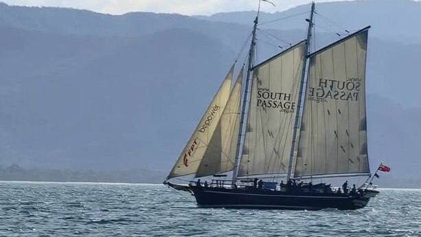 A tall ship passing a mountainous island. 