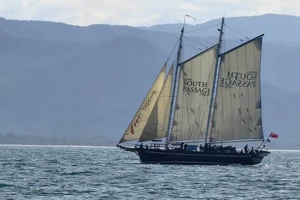 A tall ship passing a mountainous island. 