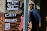 A man and a woman walk out of a building smiling, with electoral signs also visible 