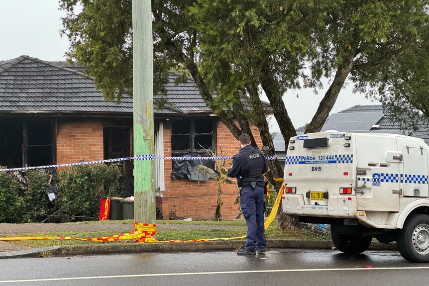 Police officer and car seen outside brick house with charred windows