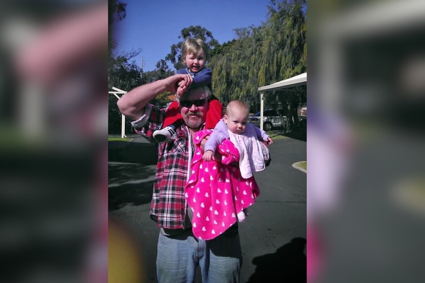 Stephen Pokrywka in a flannel shirt, holding his young grandchildren