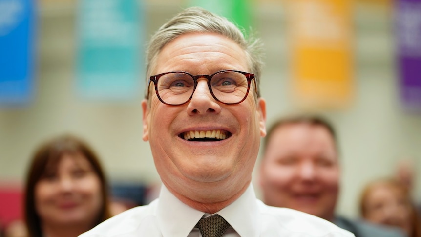 A man in a suit smiling and looking on, seen from close up.