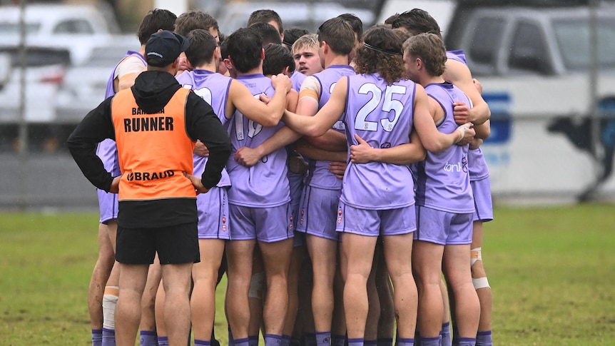 A group of football players wearing purple jumpers huddle together. 