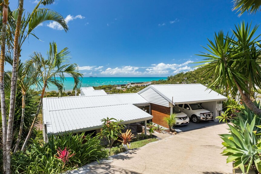 the front of a house and carport, with the ocean seen behind it