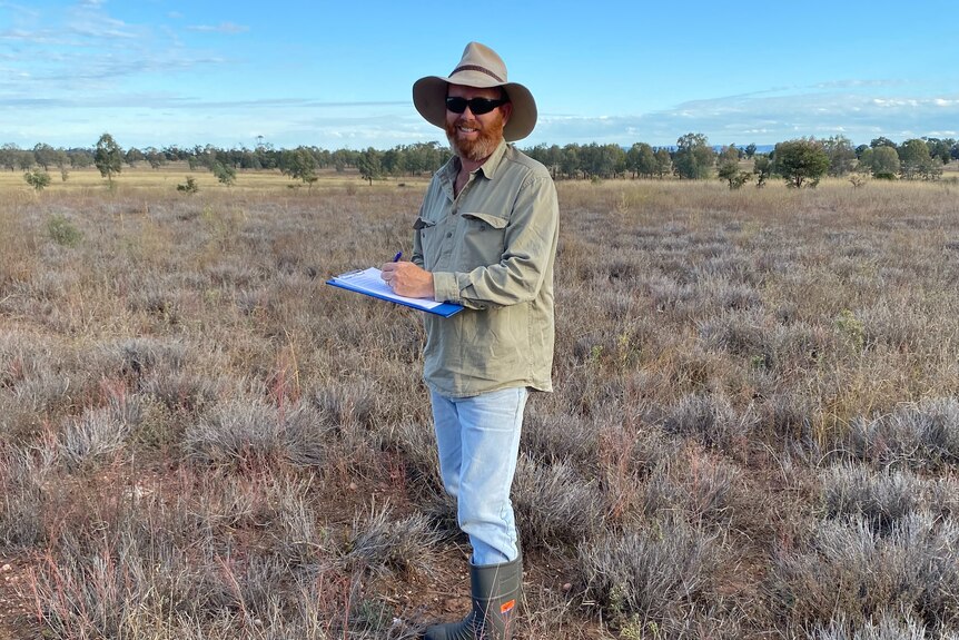 A man stands in a brown paddock.