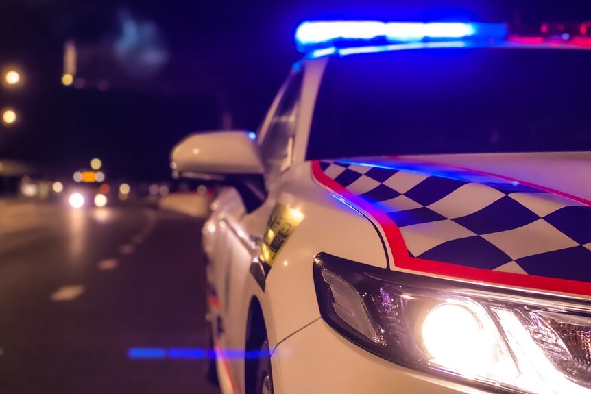 A night time photo of a Queensland Police Service car with its blue light illuminated.