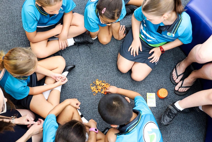 New prep-aged children sit on floor in circle in prep classroom playing barrel of monkeys game at Spring Mountain State School.