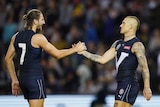 two men in dark blue AFL jumpers greet each other with hands outstretched