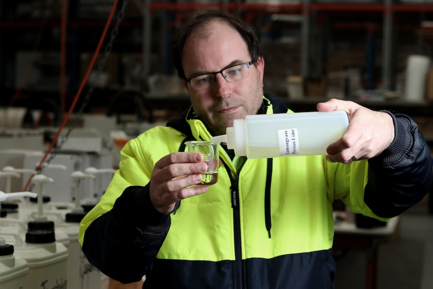 A bespectacled man with dark hair carefully pours liquid from a plastic bottle into a small beaker.