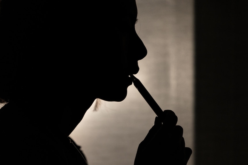 A shadowy outline holds a vape to their mouth.