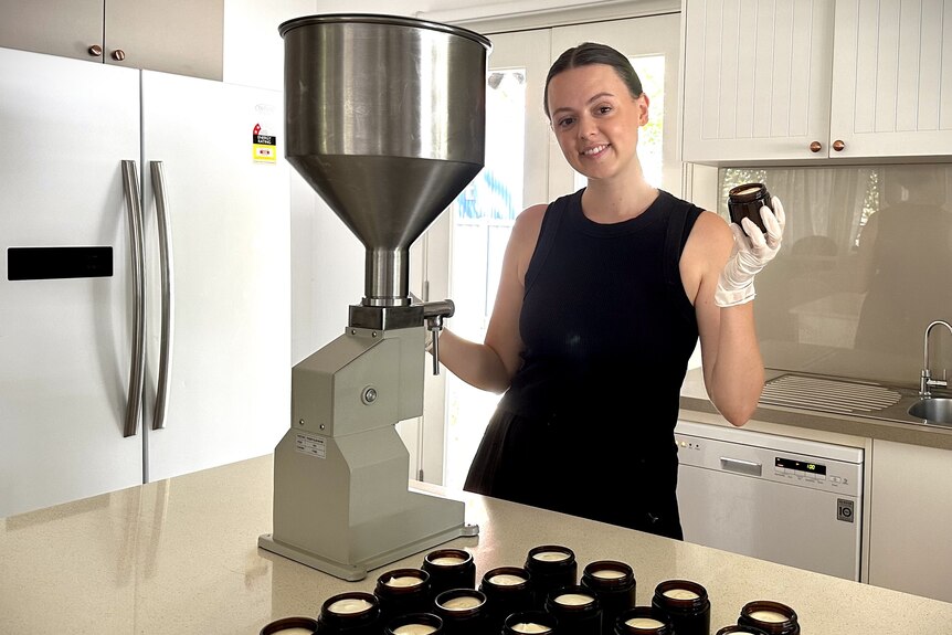 A young woman stands next to a batch of jars filled with tallow products.