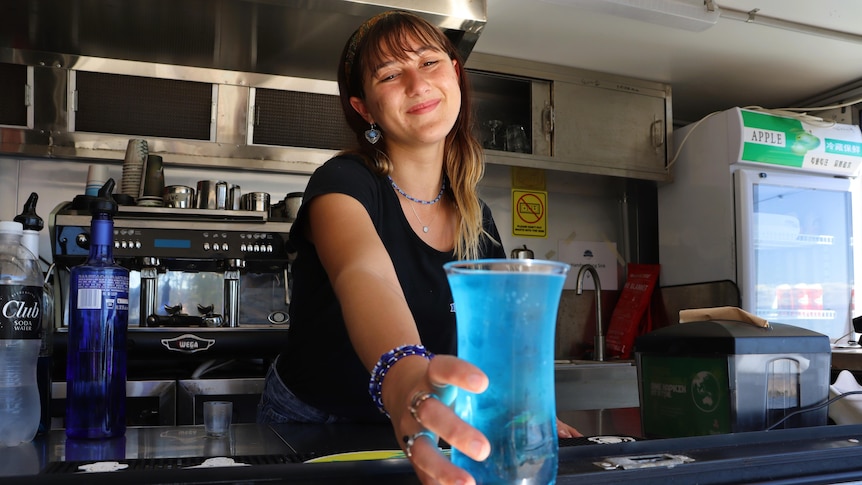 woman smiles as she puts blue drink on bench