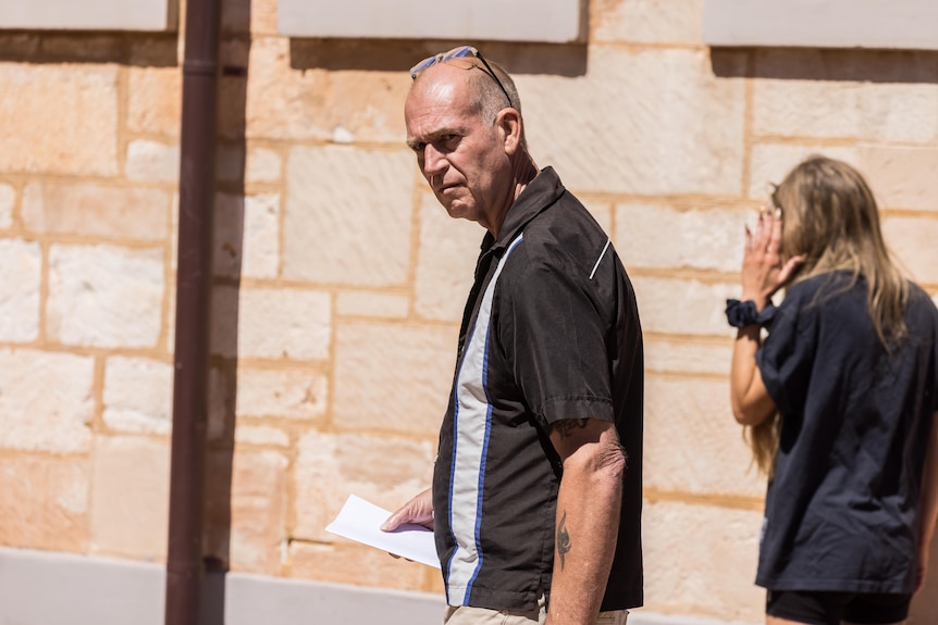 A man walking outside a courthouse while a female supporter shields her face.  