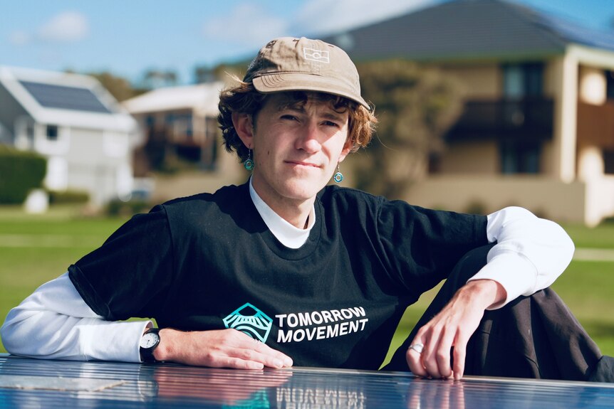 A young man wearing a cap sitting at a park table on a sunny day.