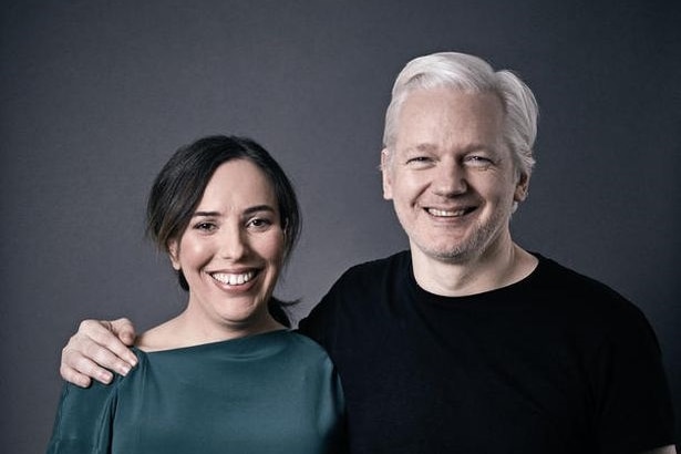 A man with white hair and a black T-shirt puts his arm around a woman with dark hair and a green top