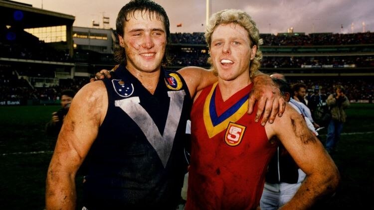 Former VFL/AFL players Tony Lockett and Dermot Brereton stand with arms around each others shoulder.