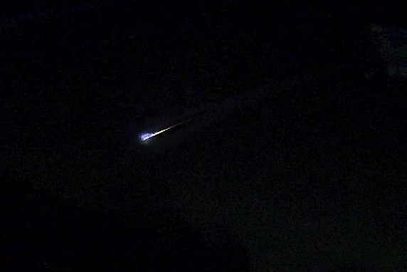 The black night sky with a blue fireball creating a streak of light.