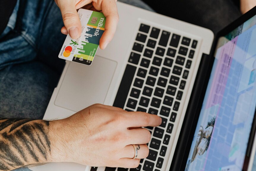 Person holding out a credit card card against their laptop