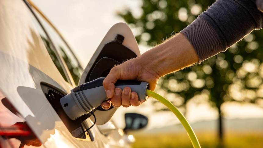 Hand of man inserting a power cord into an electric car