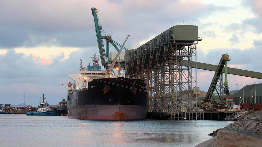 A large ship in the port with a tugboat nearby at sunset