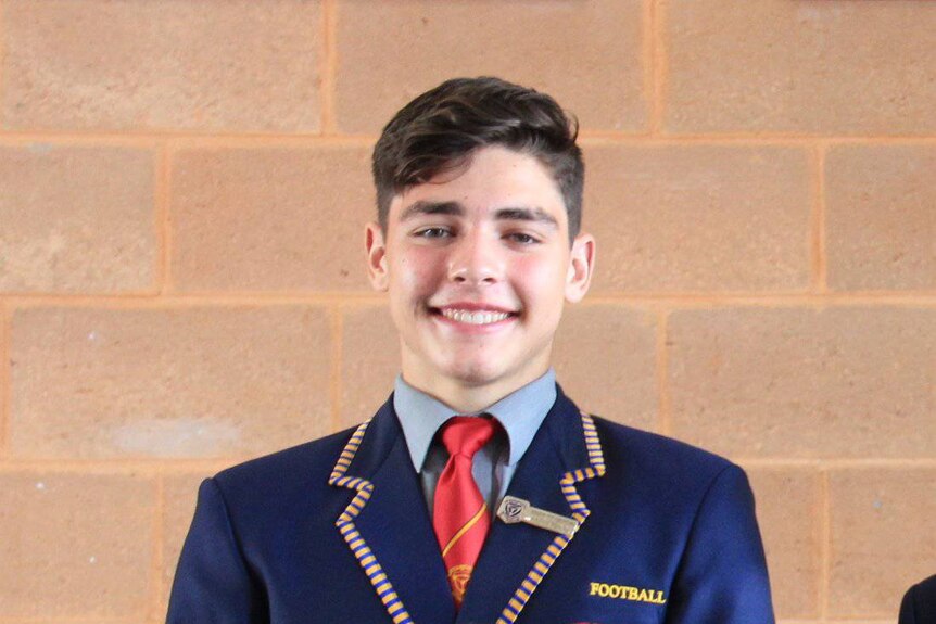 A teenager in college blazer poses for a school photo.