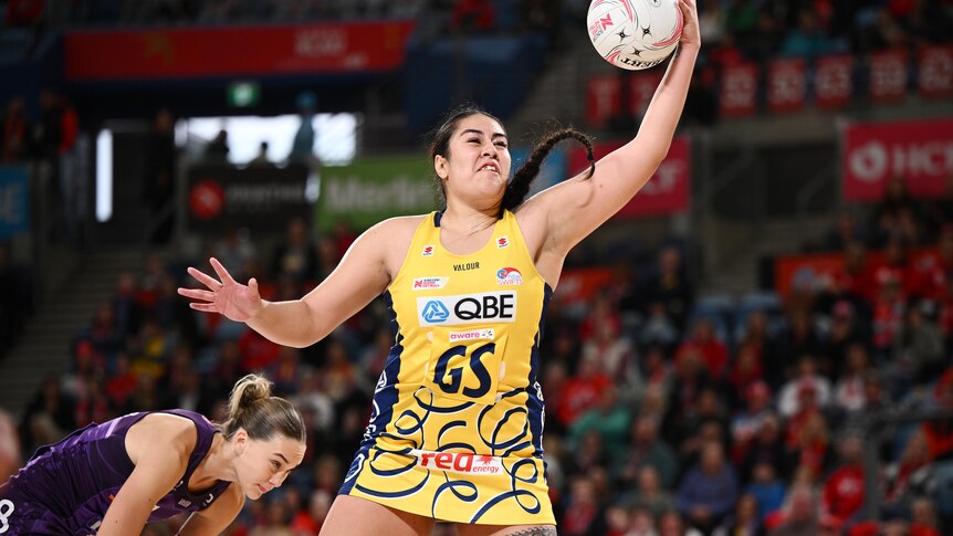 Palavi takes the ball one handed in a yellow and blue dress as the crowd watches on