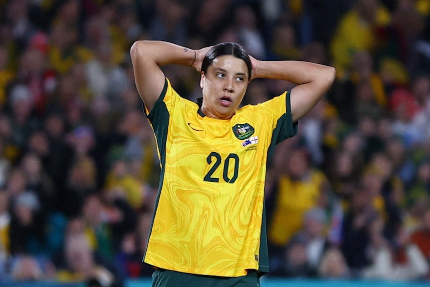 A woman looks on with her hands behind her head.