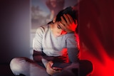 A girl sitting cross-legged looking at her phone with a worried look on her face; and her forehead in the palm of her hand