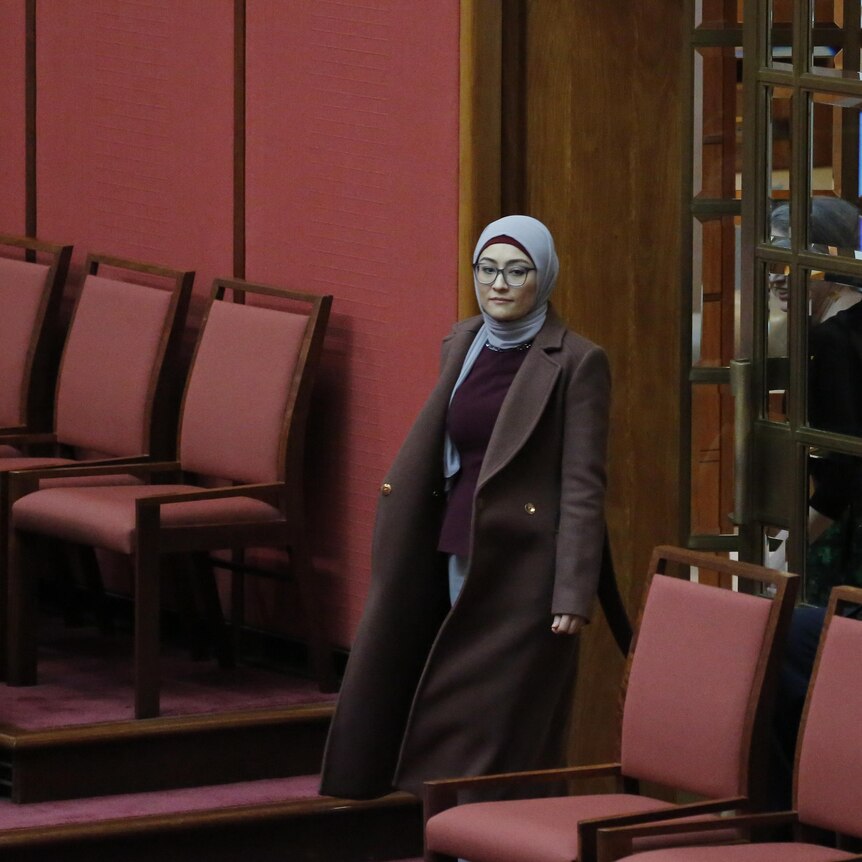 A woman in a hijab walks in the doors of the red Senate chamber.