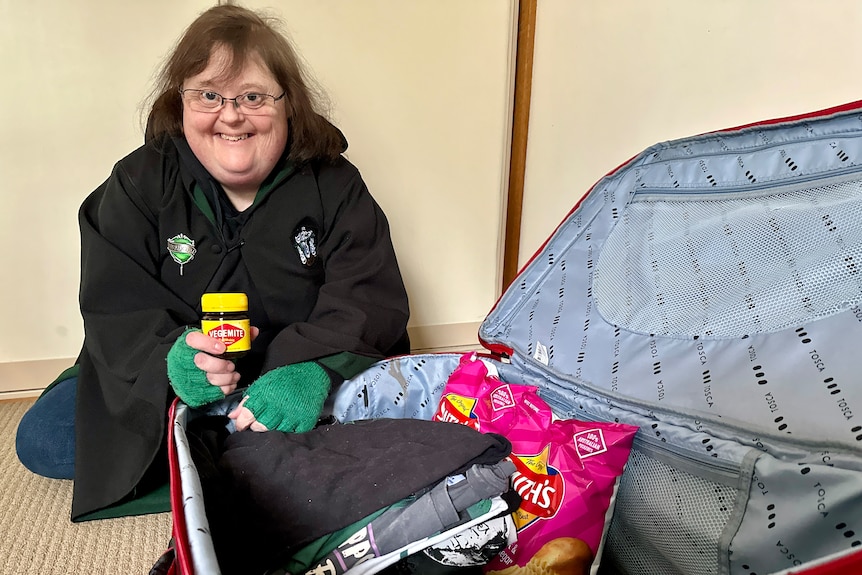 A person holding a jar of Vegemite and packing a suitcase