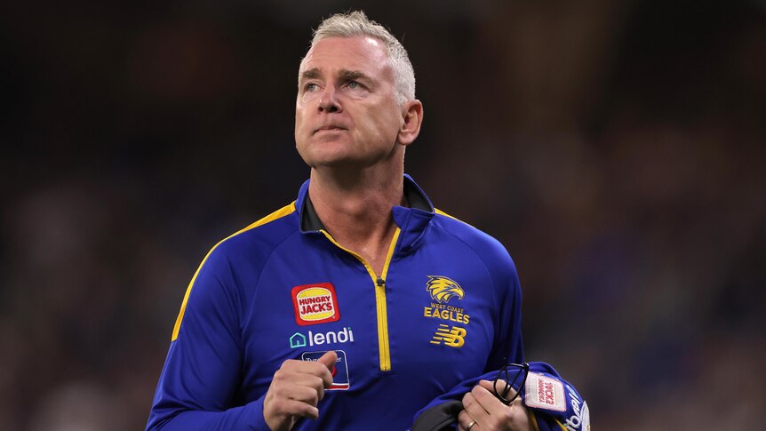 A mid-shot of West Coast Eagles coach Adam Simpson on ground with a blue and yellow team jumper on, looking upwards.