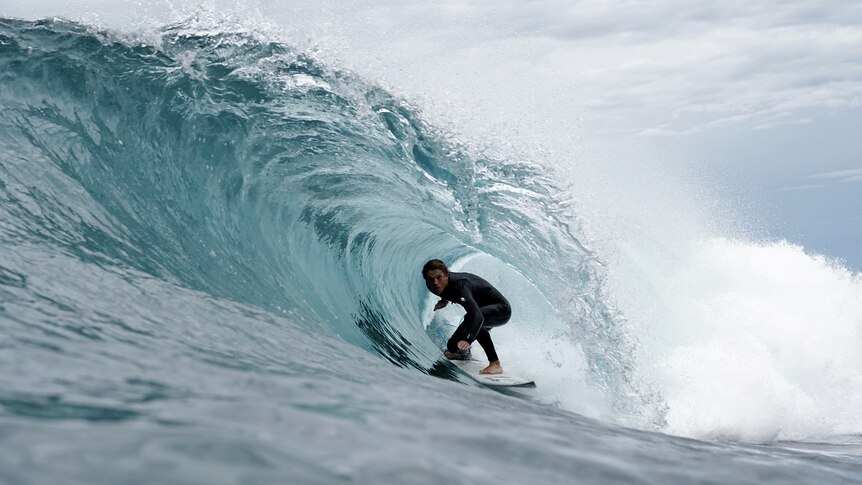 a teenager on a surfboard crouches in a tube