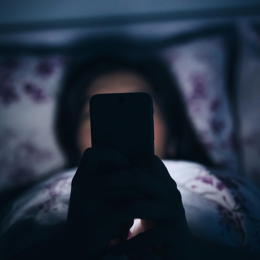 Image of a woman in bed at night scrolling on her phone. 