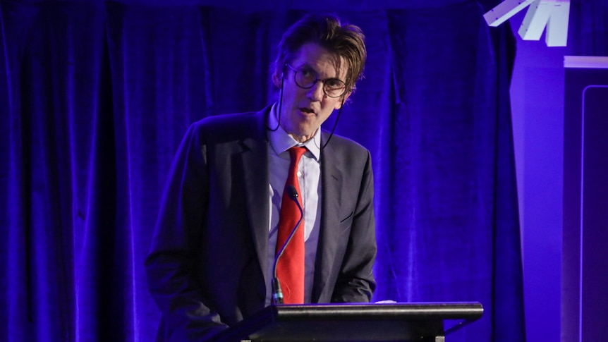 A man in a suit speaking at a lectern. 