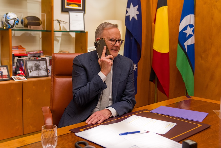 Albanese sits at his desk in parliament house, speaking on the phone.
