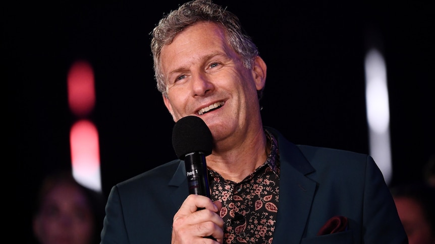 Adam Hills speaks into a microphone onstage at the ParalympicsGB Homecoming