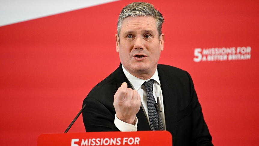 A man stands behind a lectern inside in front of a red banner that says '5 missions for a better future'