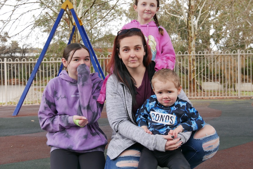 A woman with her three children sitting in playground.