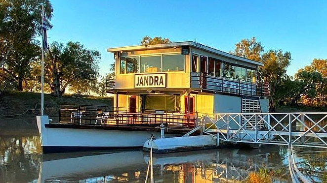 A paddle steamer tied up at a jetty on a river, with blue sky overhead.