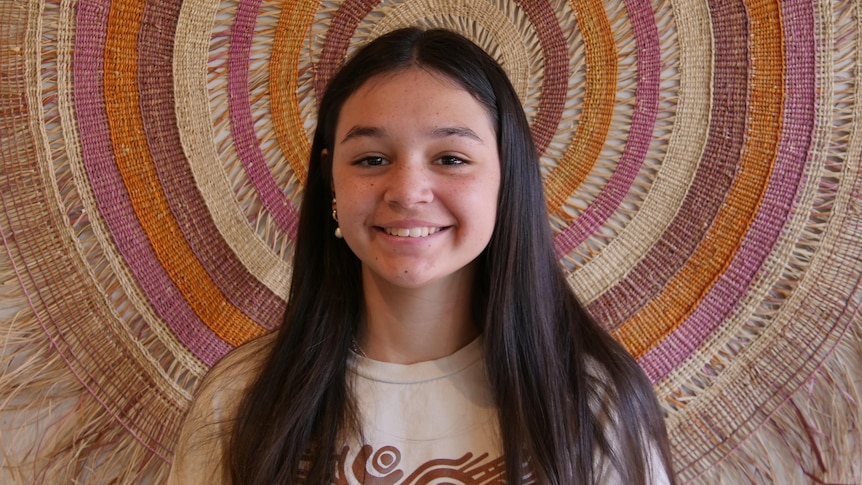 young girl stands behind an indigenous wall hanging 